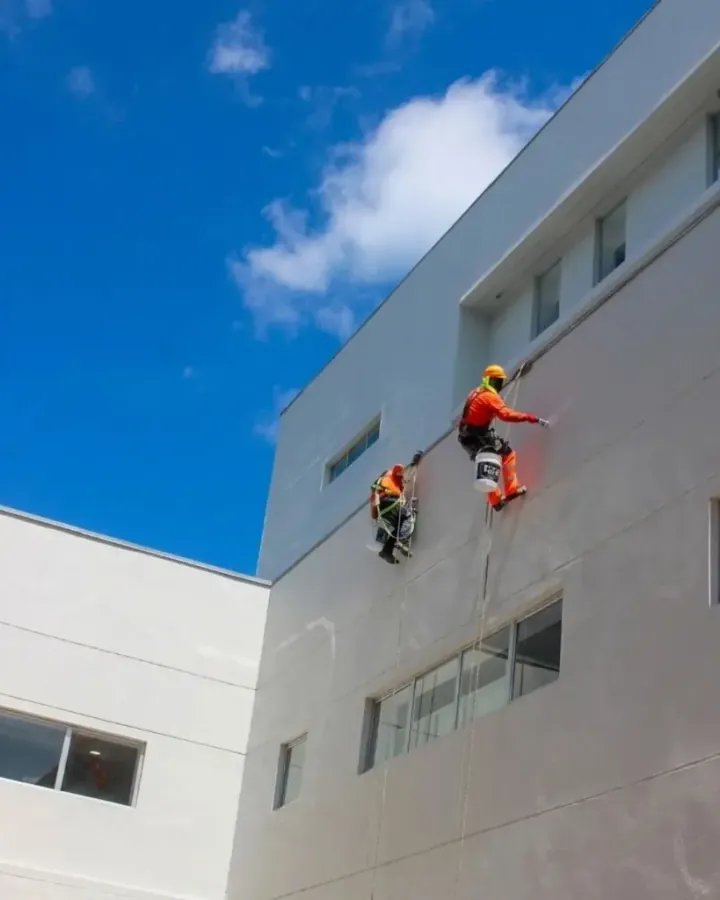 Pintores en arnés aplicando recubrimiento impermeable en muro